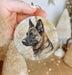 a hand holding a christmas ornament with a german shepherd picture on it