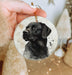 a hand holding a black dog ornament in front of a christmas tree