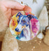 a hand holding a round ornament with a dog's face painted on
