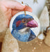 a hand holding a christmas ornament with a blue bird on it
