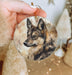 a hand holding a round ornament with a picture of a wolf on it