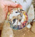 a hand holding a round ornament with a dog on it