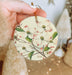 a person holding a christmas ornament with flowers on it
