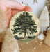 a person holding a christmas ornament with a tree on it
