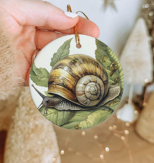 a hand holding a christmas ornament with a snail on it