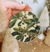 a person holding a christmas ornament with berries and leaves on it