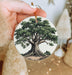 a person holding a christmas ornament with a tree on it