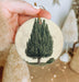 a hand holding a christmas ornament with a tree on it
