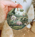 a person holding a round ornament with a painting of flowers