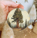 a person holding a christmas ornament with a tree on it