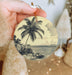 a person holding a christmas ornament with a palm tree on it
