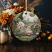 a ceramic ornament with a painting of a pond surrounded by flowers