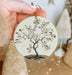 a hand holding a ceramic ornament with a tree on it