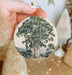 a person holding a christmas ornament with a tree on it