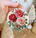 a person holding a christmas ornament with roses on it