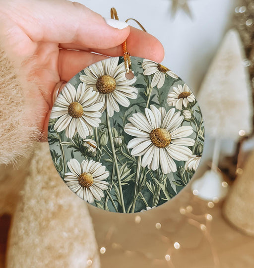a hand holding a white flower ornament in front of a christmas tree