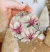 a person holding a christmas ornament with pink flowers on it