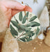 a person holding a round ornament with leaves on it