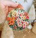 a person holding a christmas ornament with flowers on it