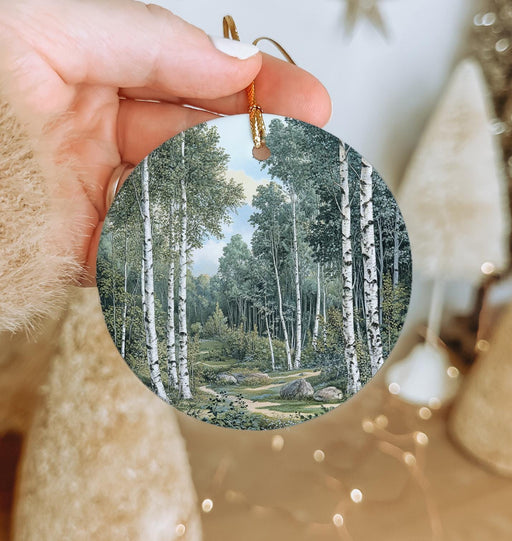 a hand holding a round ornament with a painting of a forest