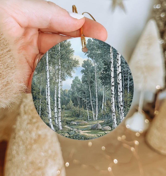 a hand holding a round ornament with a painting of a forest