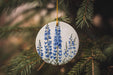 a ceramic ornament with blue flowers hanging from a tree
