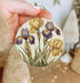 a hand holding a round ornament with flowers painted on it