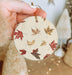 a person holding a christmas ornament with leaves on it