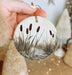 a hand holding a christmas ornament with a painting on it