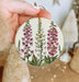 a hand holding a christmas ornament with pink flowers