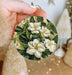 a hand holding a christmas ornament with white flowers