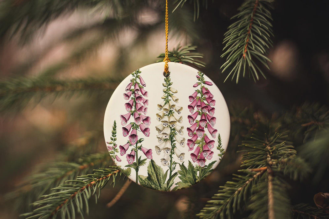 a ceramic ornament with pink flowers hanging from a pine tree