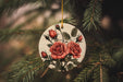 a ceramic ornament with red roses hanging from a tree