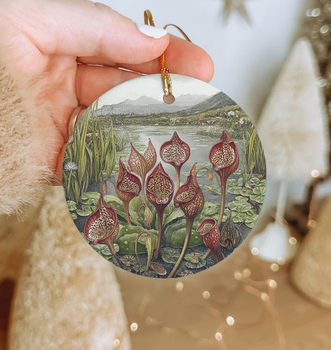 a hand holding a christmas ornament with a painting of flowers
