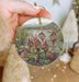 a hand holding a christmas ornament with a painting of flowers