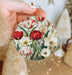 a person holding a christmas ornament with flowers on it