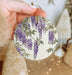 a hand holding a ceramic ornament with purple flowers