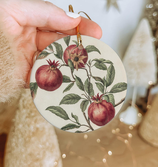 a hand holding a christmas ornament with pomegranates on it