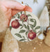 a hand holding a christmas ornament with pomegranates on it