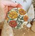 a hand holding a yellow and orange flower ornament
