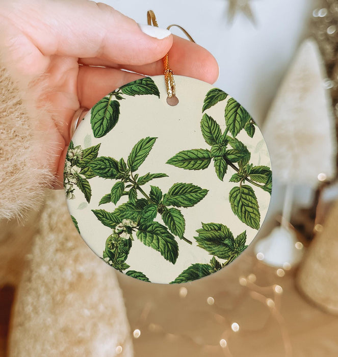 a hand holding a round ornament with green leaves on it