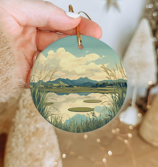 a hand holding a round ornament with a lake scene on it