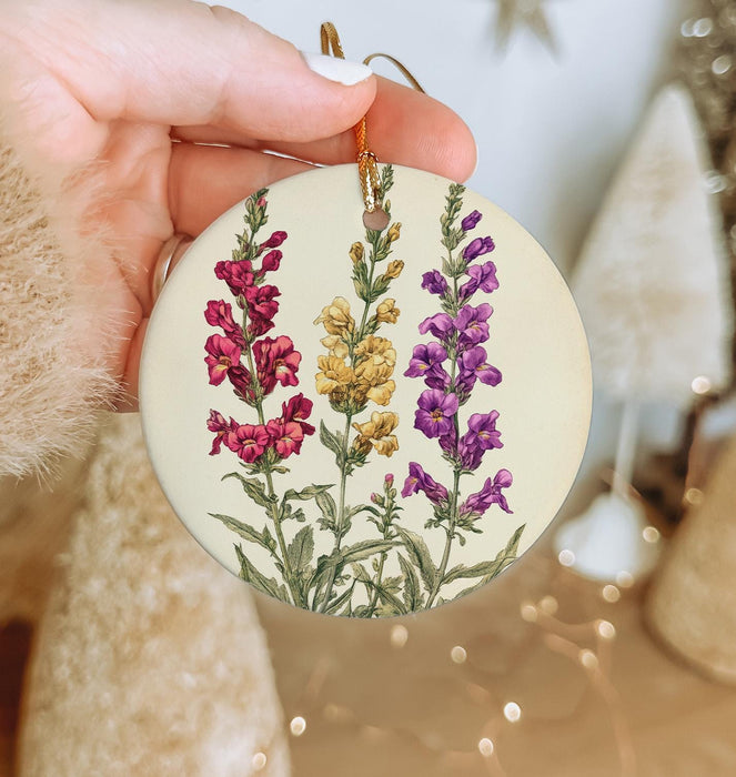 a hand holding a round ornament with flowers painted on it
