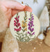 a hand holding a round ornament with flowers painted on it