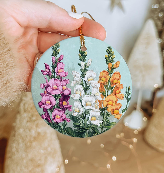 a hand holding a round ornament with flowers painted on it