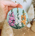 a hand holding a round ornament with flowers painted on it