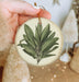 a person holding a christmas ornament with a green plant on it