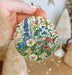 a hand holding a round ornament with flowers on it