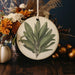 a picture of a green leaf on a white ornament
