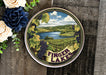 a tint tin with a painting of a lake surrounded by flowers